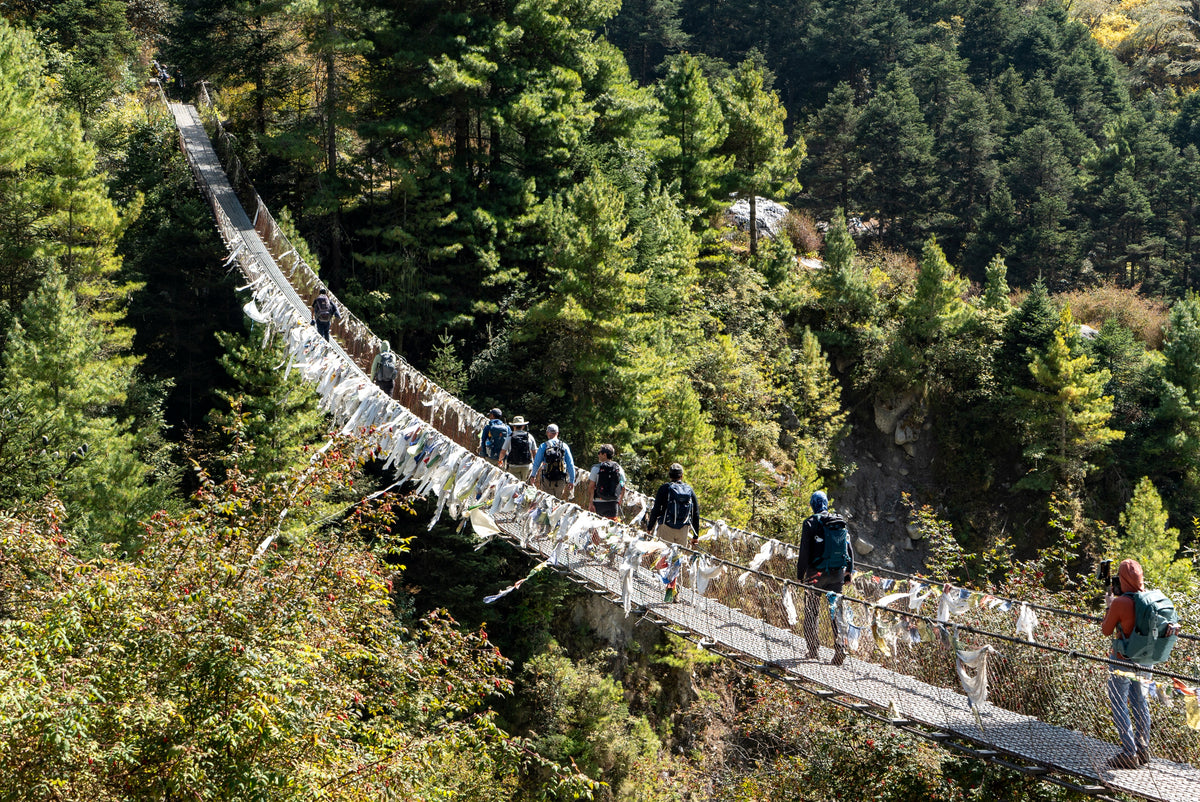 Trekkers crossing a suspension bridge hung with prayer flags in the Everest region of Nepal