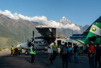 Small airplane on a tarmac with people and vehicles, mountainous landscape in the background