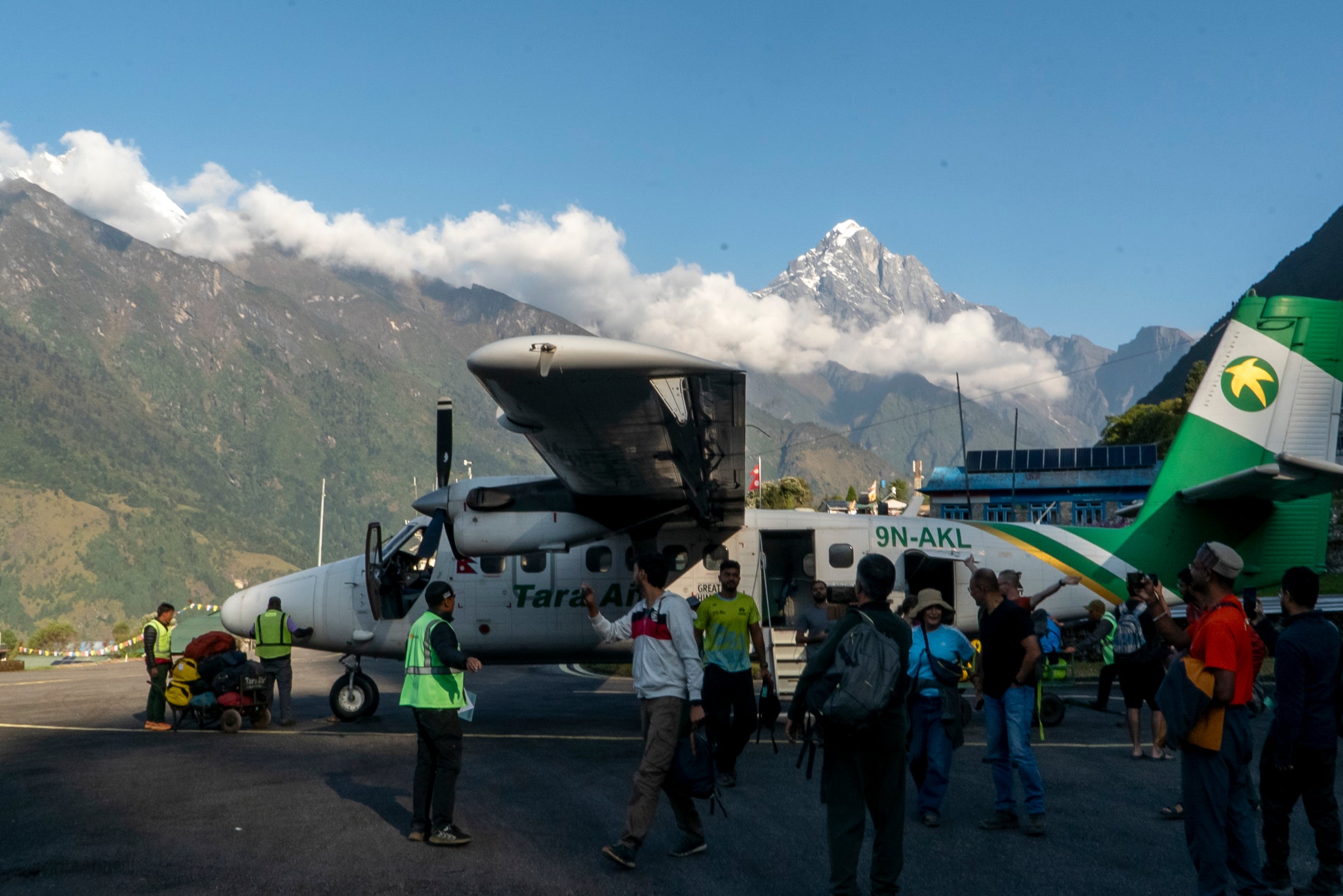 Small airplane on a tarmac with people and vehicles, mountainous landscape in the background