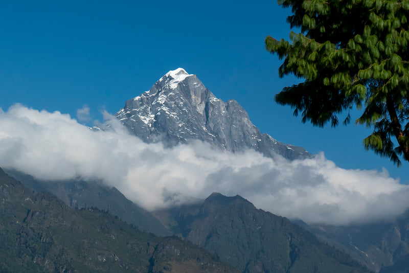 Mountain peak with snow cover surrounded by clouds and greenery