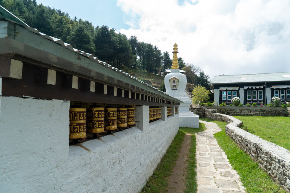 A row of prayer wheels along a stone path to a white stupa in the Khumbu