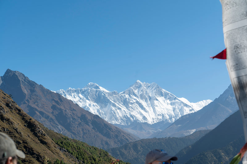 Snow-capped mountain range with a clear blue sky, people at the bottom, and a flag on the right.