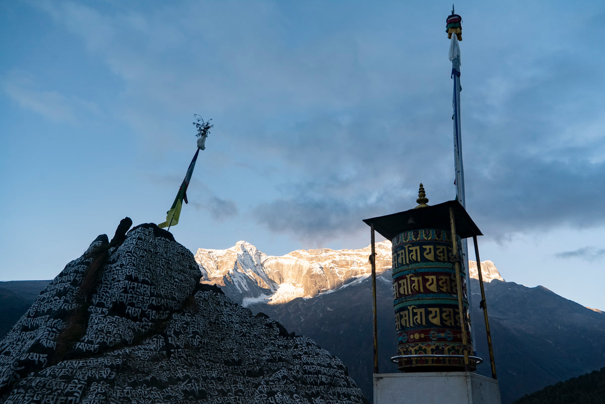A prayer wheel and a carved mani stone in the Everest region, with snow peaks behind