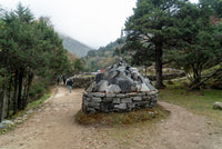 Stone cairn on a dirt path with trees and mountains in the background