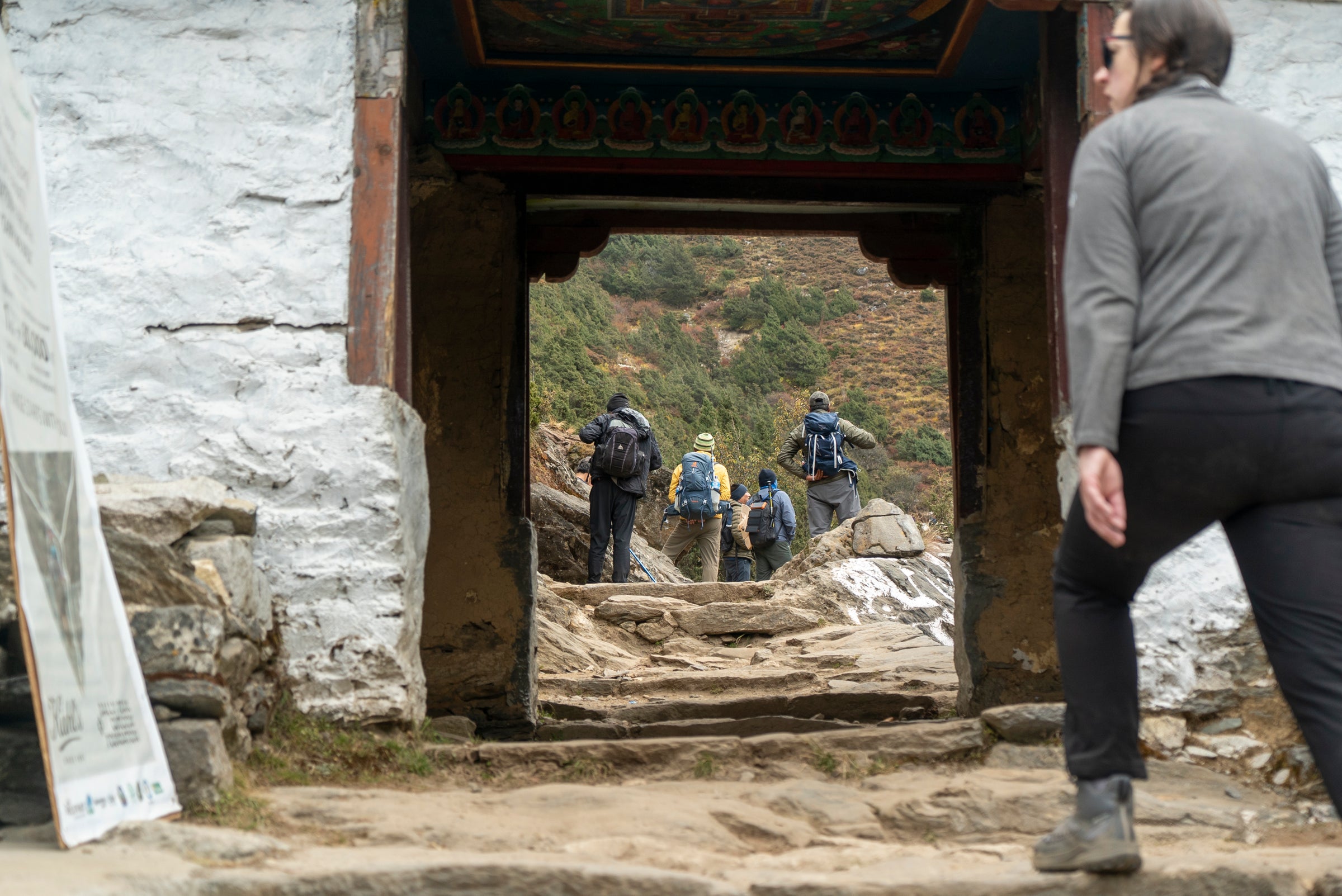People walking through a traditional wooden doorway in a mountainous area.