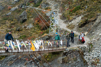 Group of people on a mountain path with a metal structure and colorful banners.