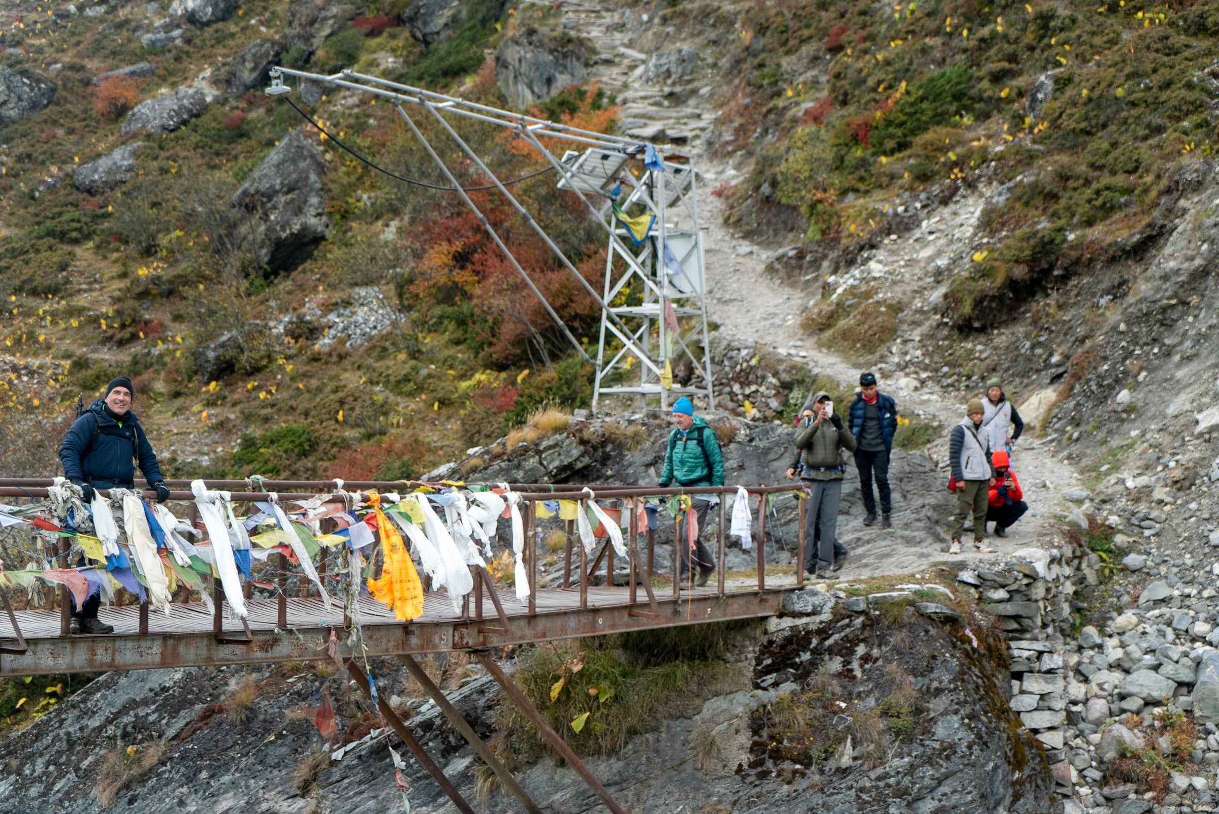 Group of people on a mountain path with a metal structure and colorful banners.