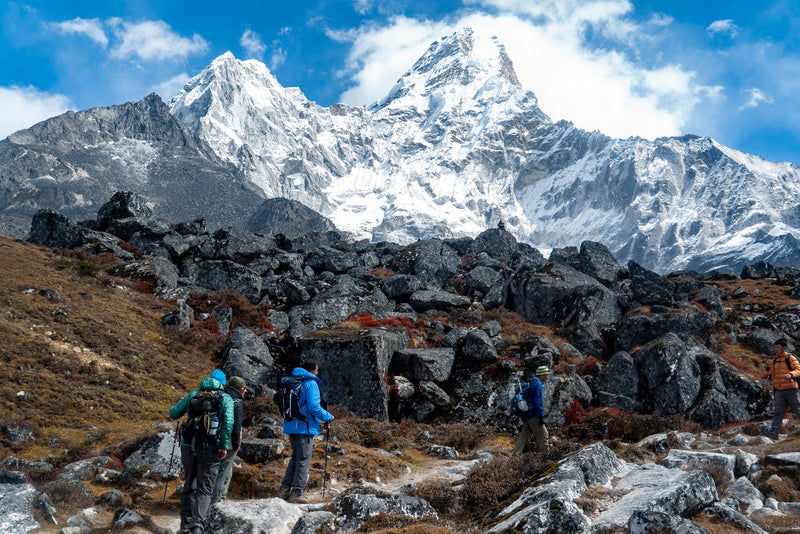 Three hikers with backpacks in a mountainous landscape with snow-capped peaks.