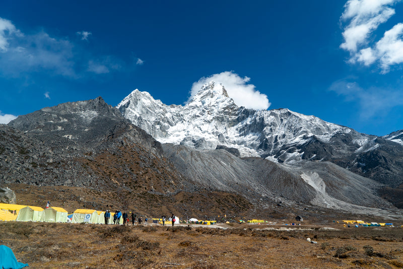 Snow-capped mountain with tents and people at a base camp in the foreground