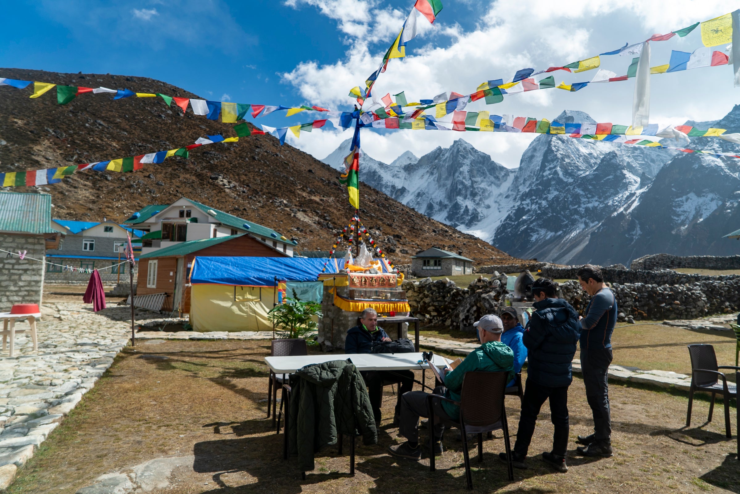 People sitting at a table with prayer flags and mountain view in the background