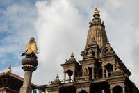 Traditional Nepalese temple with a statue on a pedestal against a cloudy sky.