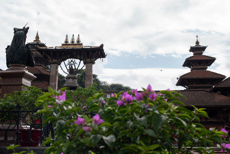 Statue and architectural structures with flowers in the foreground under a cloudy sky