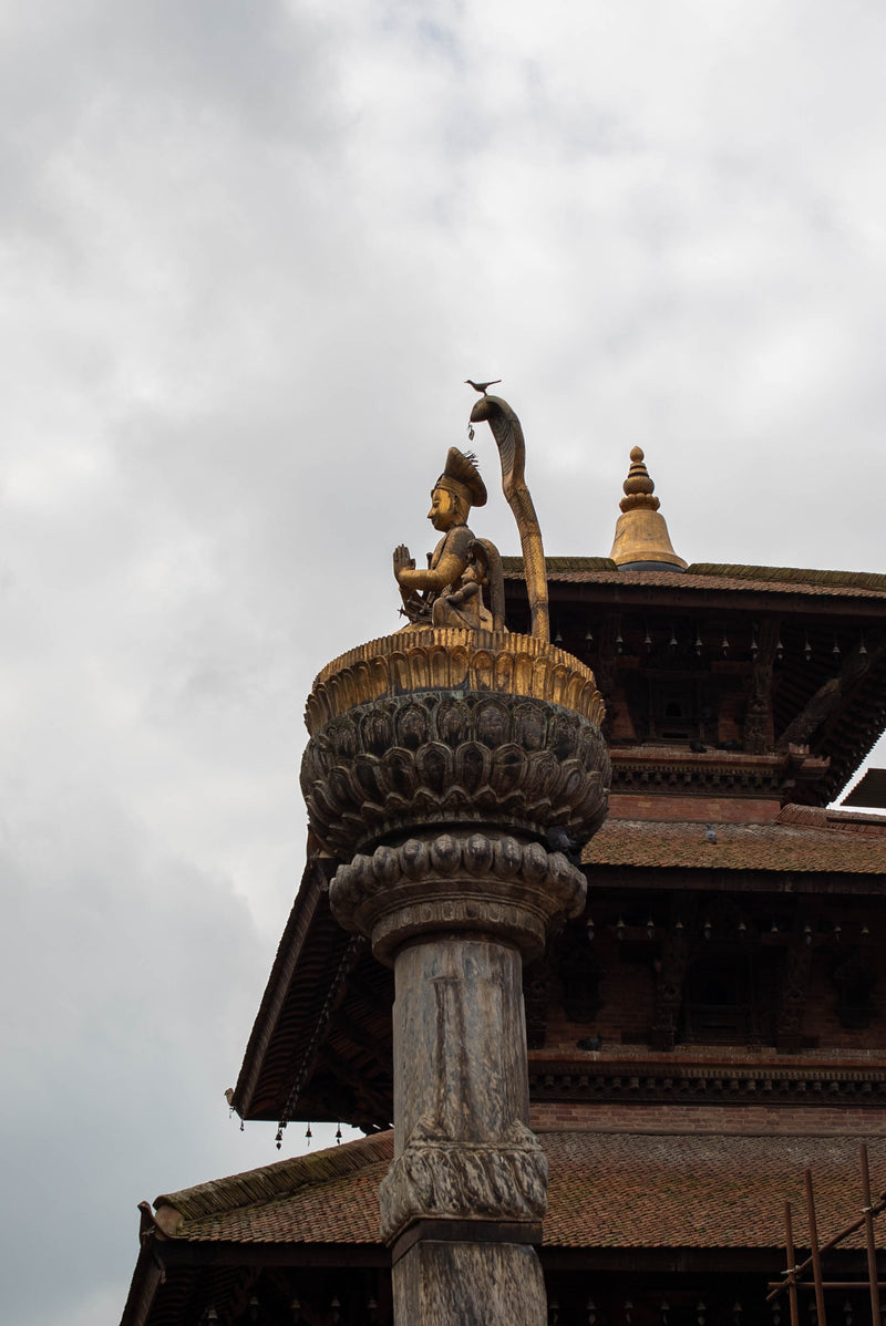 Decorative architectural element with a statue on top against a cloudy sky