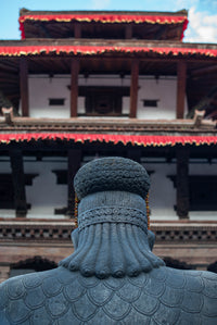 Statue with intricate detailing in front of a traditional building with red roof