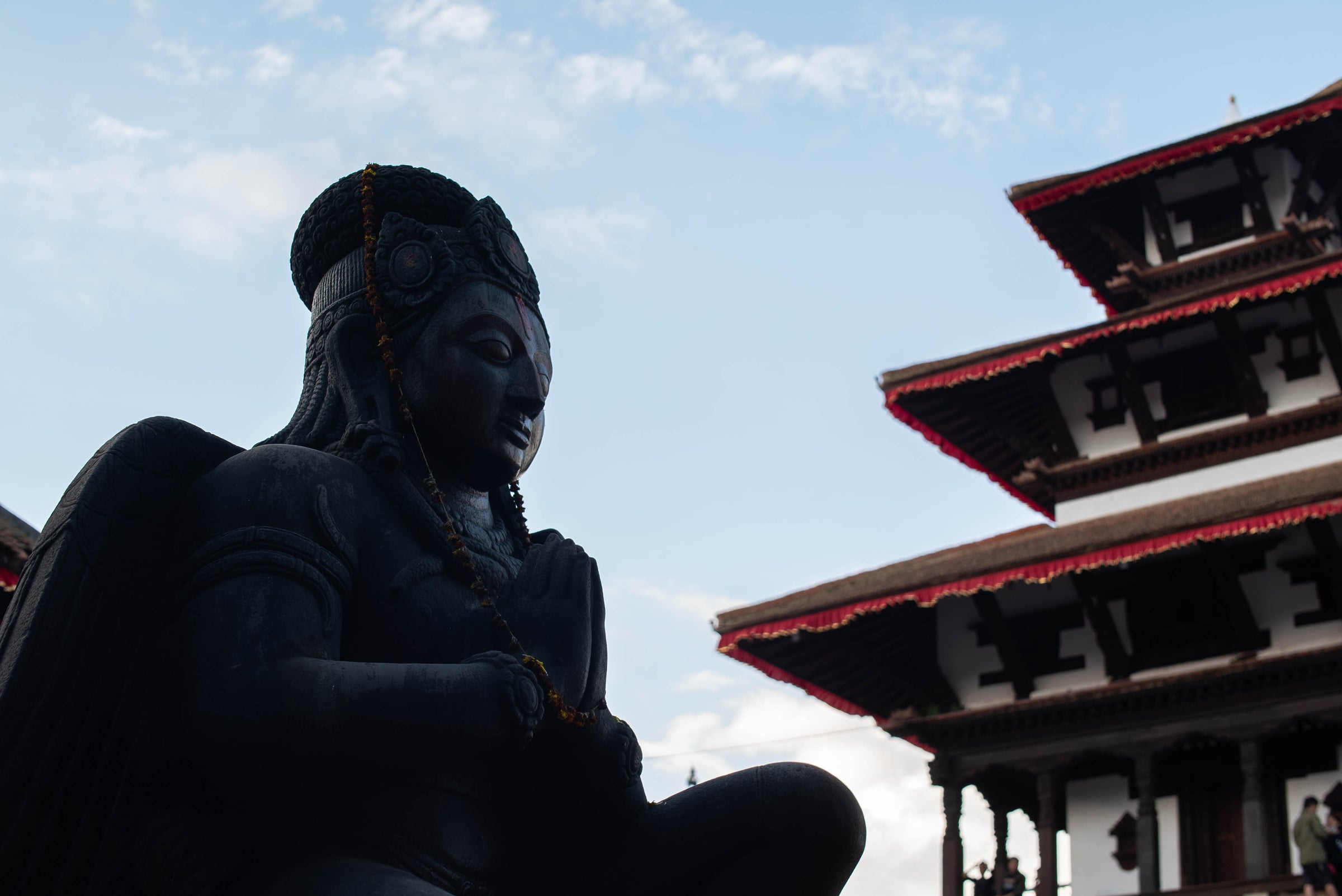 Silhouette of a statue against a clear blue sky with a traditional building in the background.