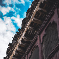 Decorative wooden eave with intricate carvings against a blue sky