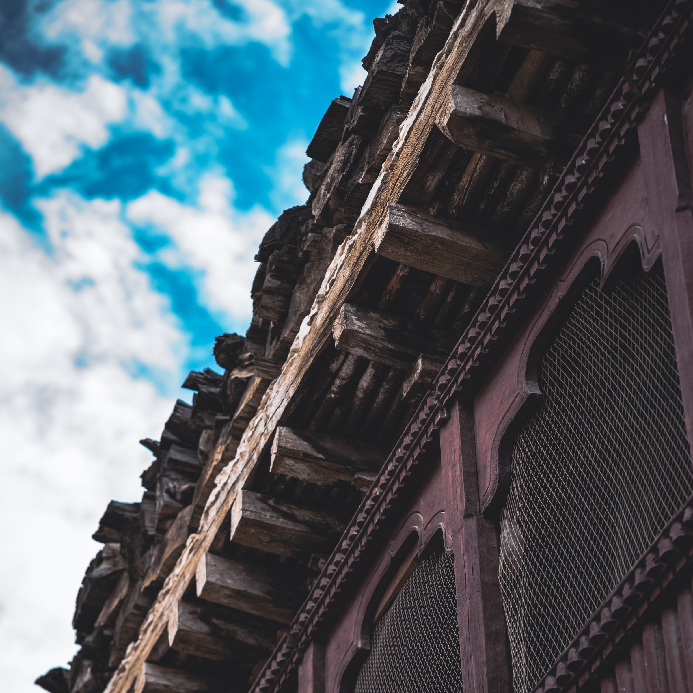 Decorative wooden eave with intricate carvings against a blue sky