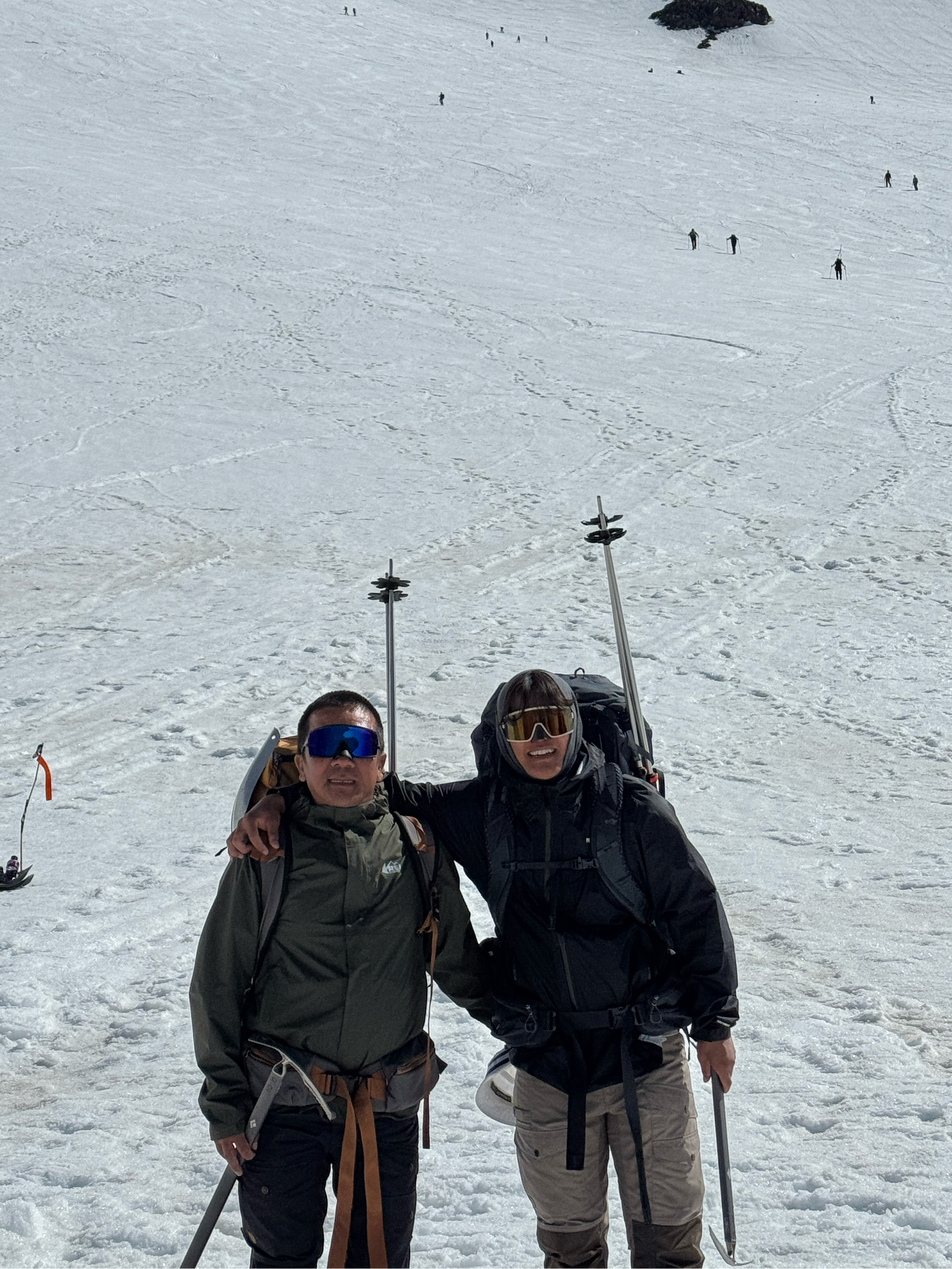 Two sherpas standing on a snowy mountain with skis and backpacks.