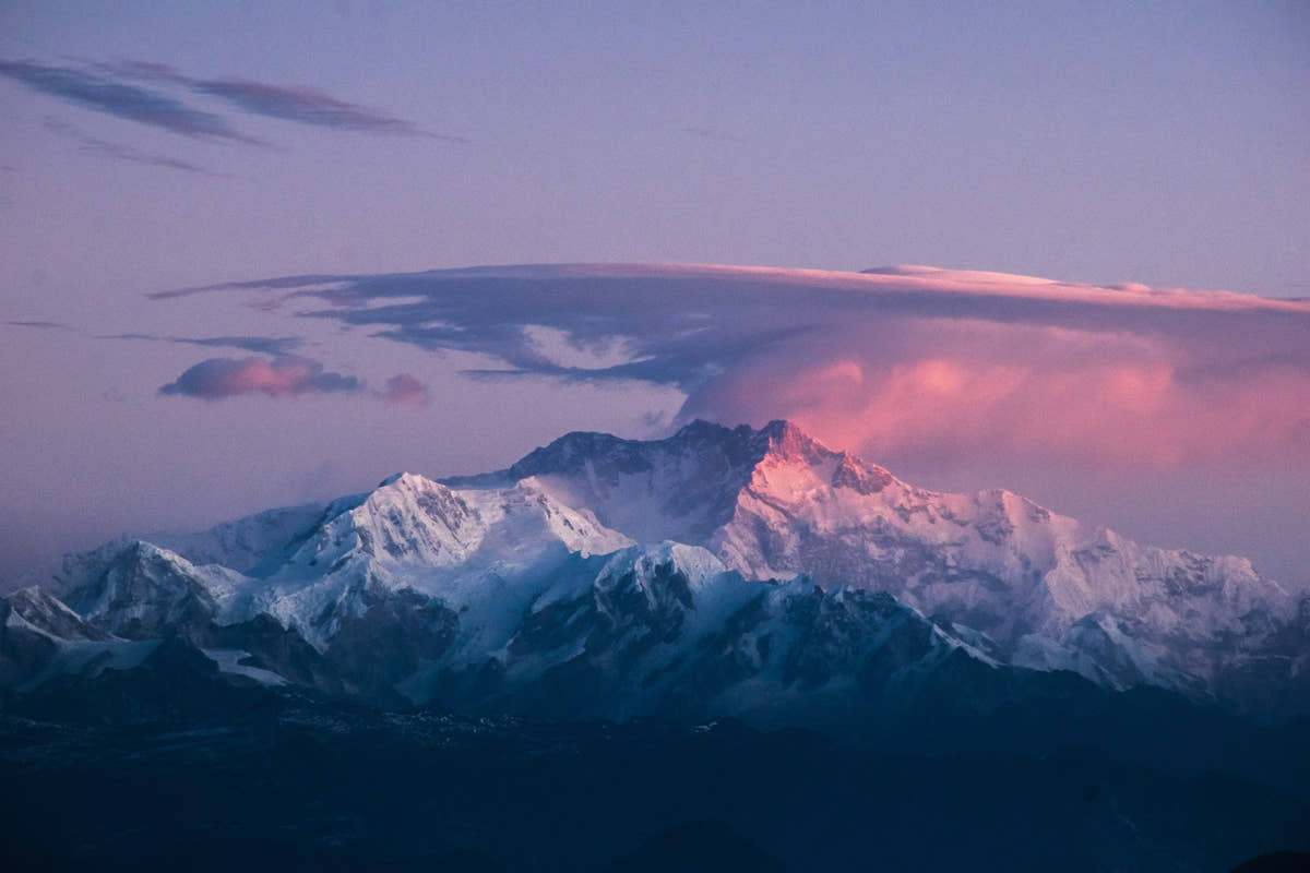 Snow-capped mountains with a pinkish hue on a cloud-covered sky