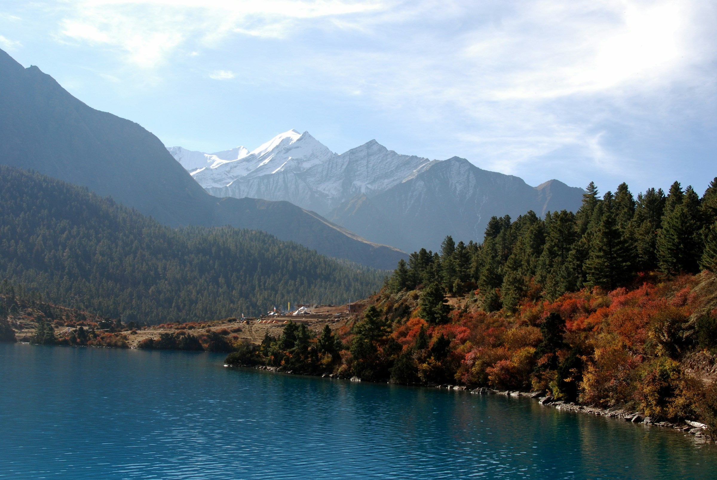 Turquoise mountain lake ringed by pine forest and autumn shrubs below snow peaks