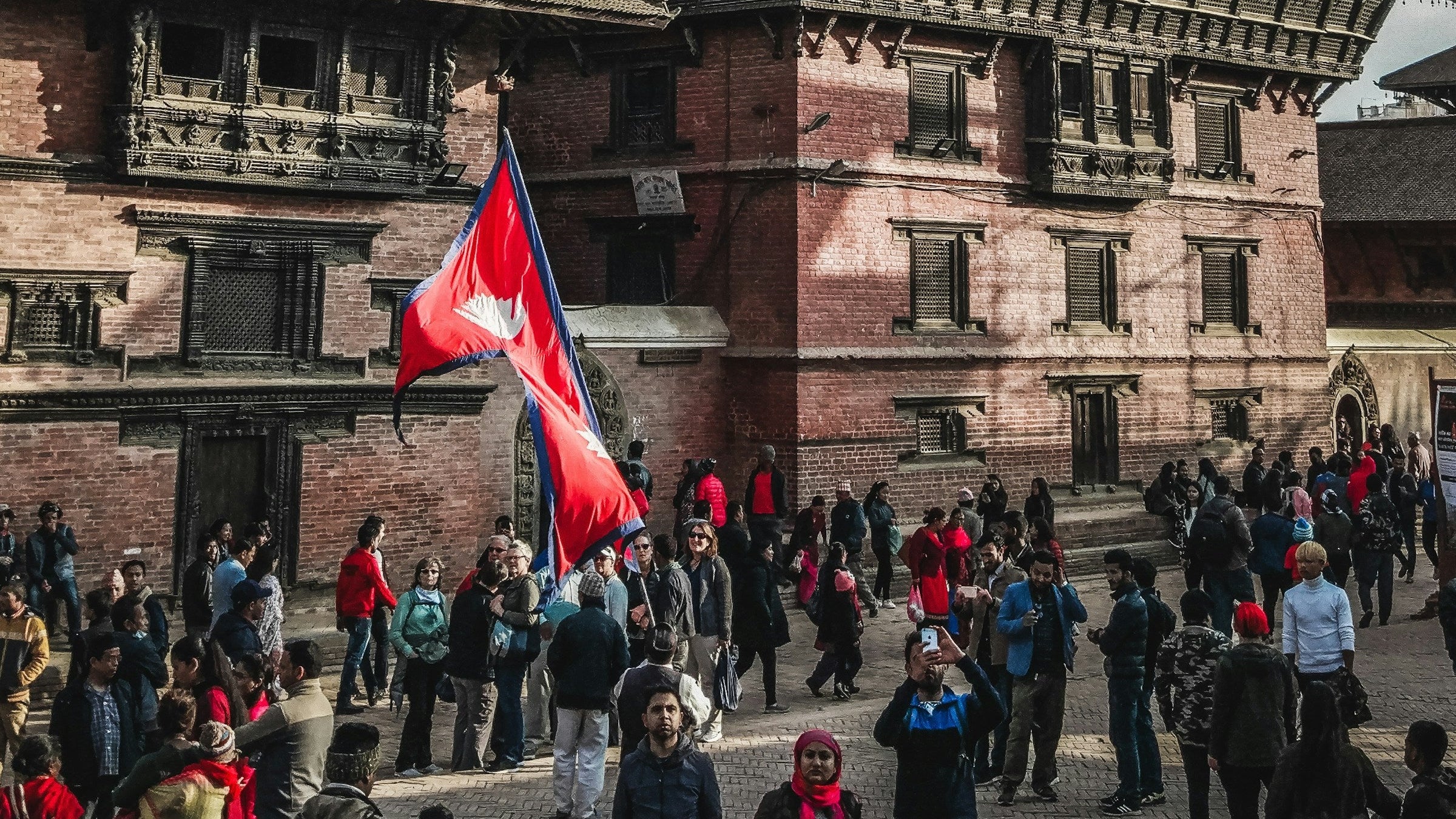 People with a red flag in front of a brick building