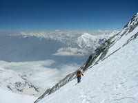 Person climbing a snow-covered mountain with a vast landscape in the background