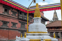 White stupa with gold accents in front of a red building with traditional architecture