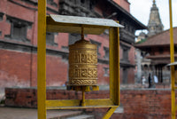 Gold prayer wheel in front of a traditional building with a blurred background