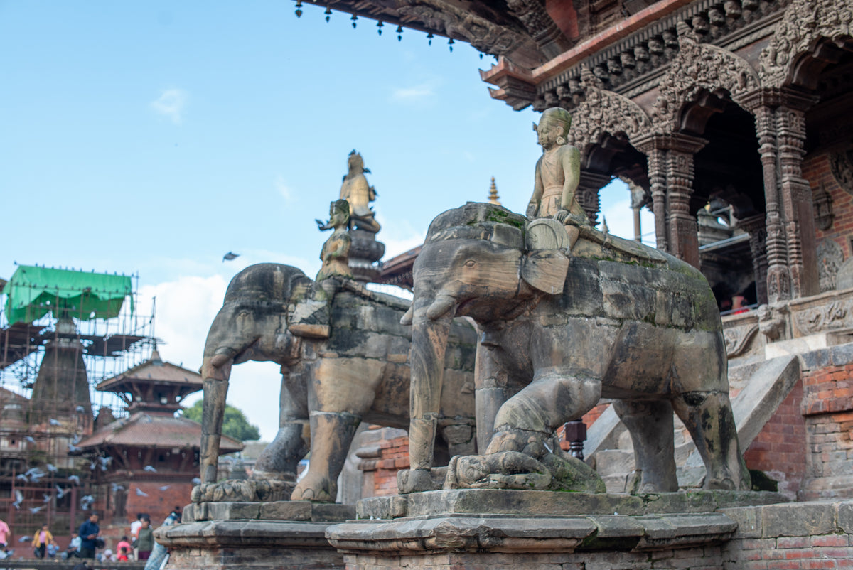 Stone elephants with riders on a temple platform under a clear blue sky.