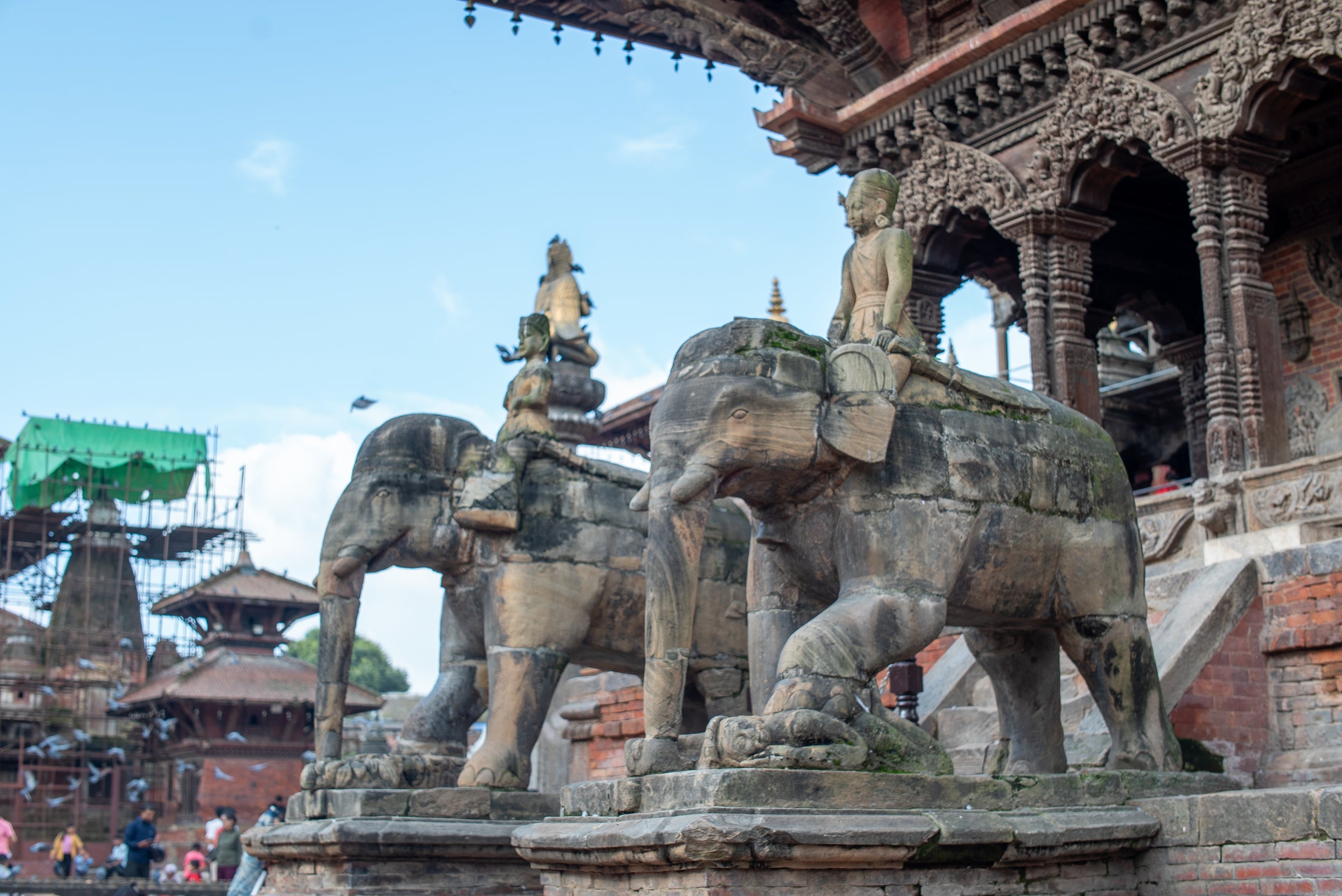 Stone elephants with riders on a temple platform under a clear blue sky.