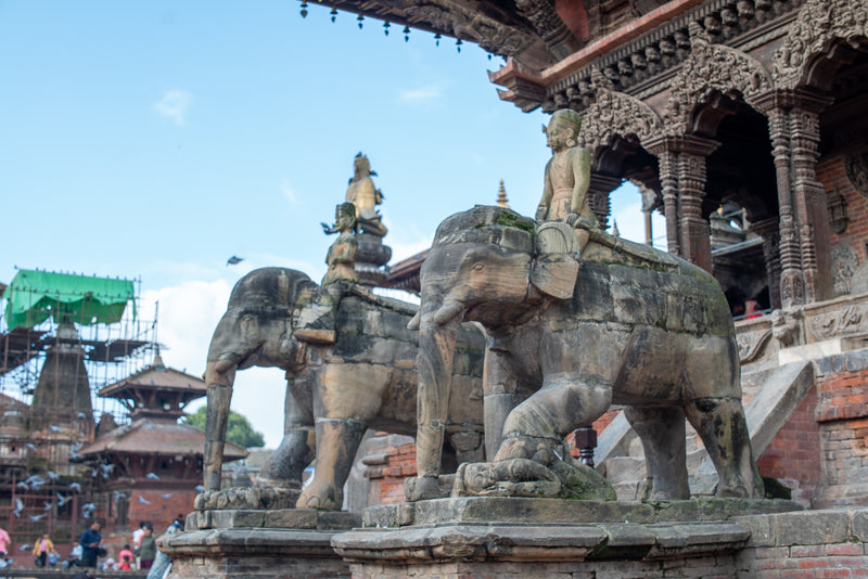 Stone elephants with riders on a temple platform under a clear blue sky.