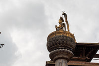 Decorative architectural element with a statue on top against a cloudy sky