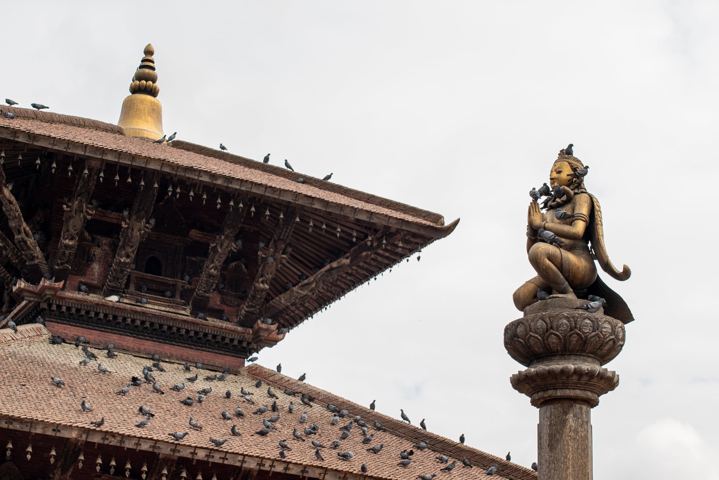 Traditional Nepalese temple with a statue on a pedestal and birds perched on the roof.