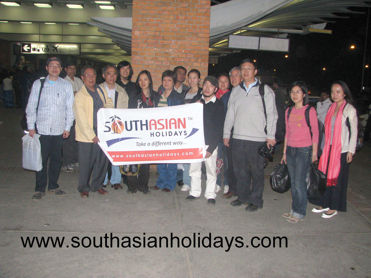 A travel group at Kathmandu airport at night, holding a South Asian Holidays banner