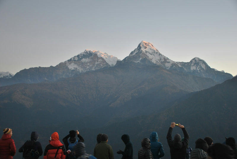 People observing a snow-capped mountain peak in a mountain range