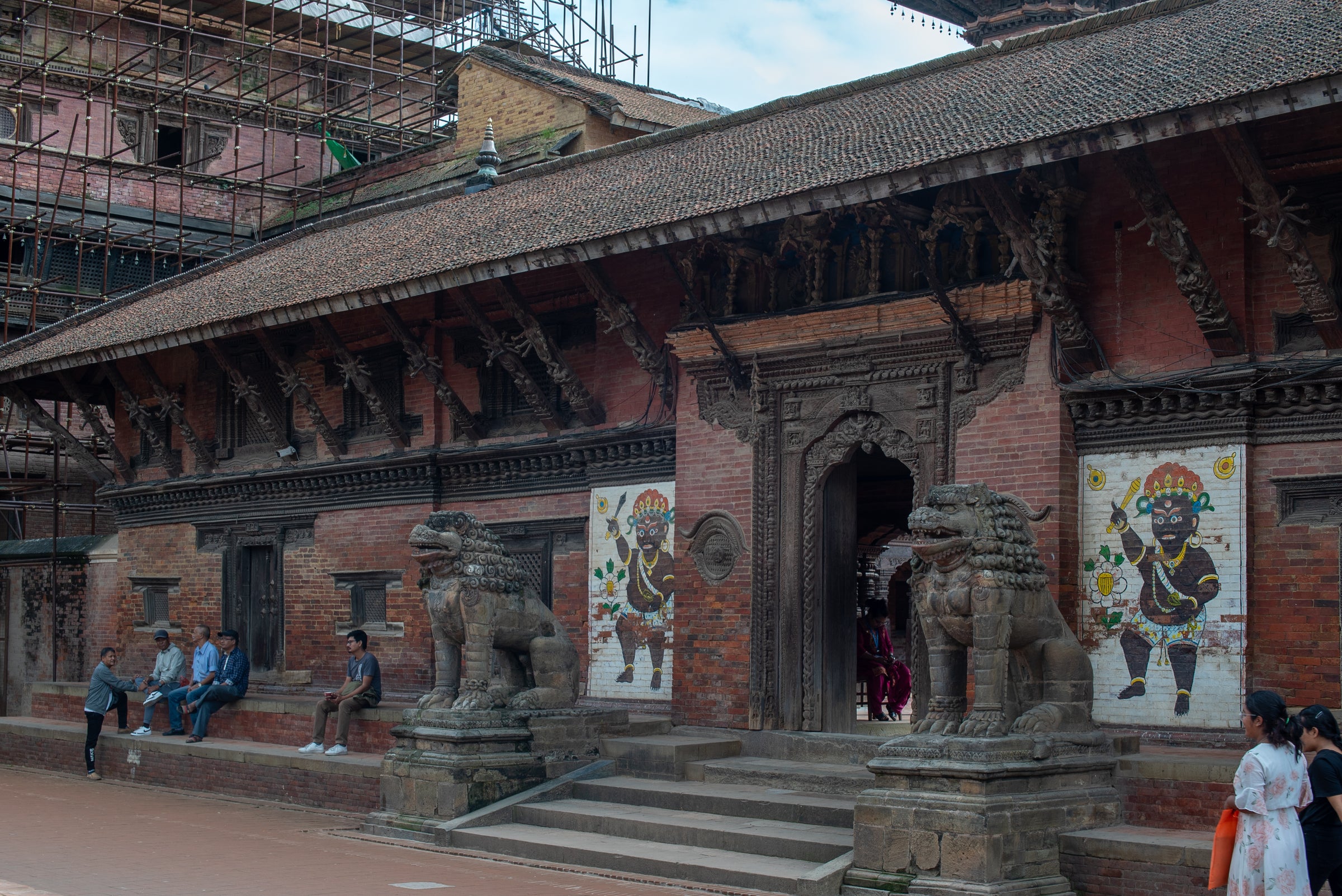 Stone lion guardians and painted murals at a temple entrance in Patan, Kathmandu Valley